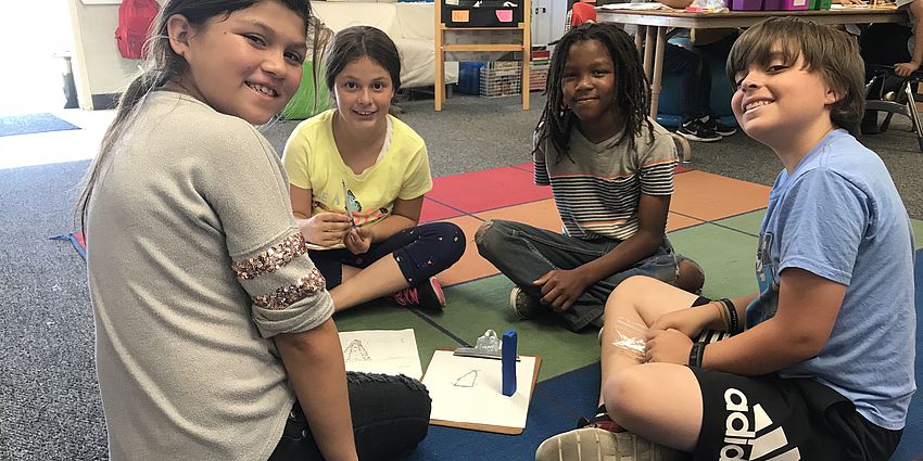 4 students sitting on floor, smiling at camera