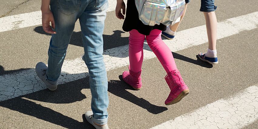 feet and legs of three children waking in the crosswalk of a street