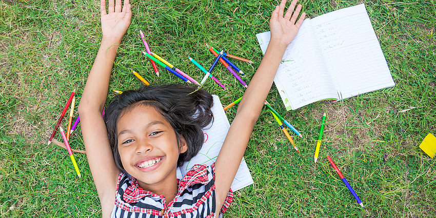 smiling girl in grass with crayons and paper