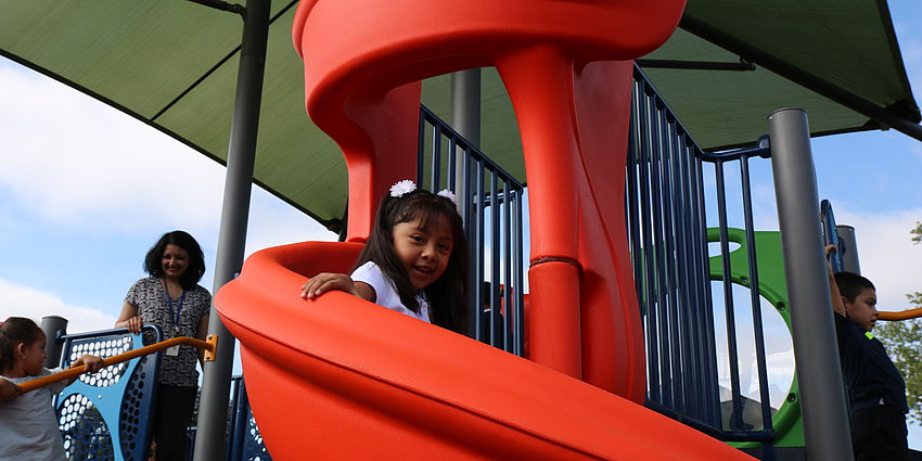 child goes down slide as adult supervises play