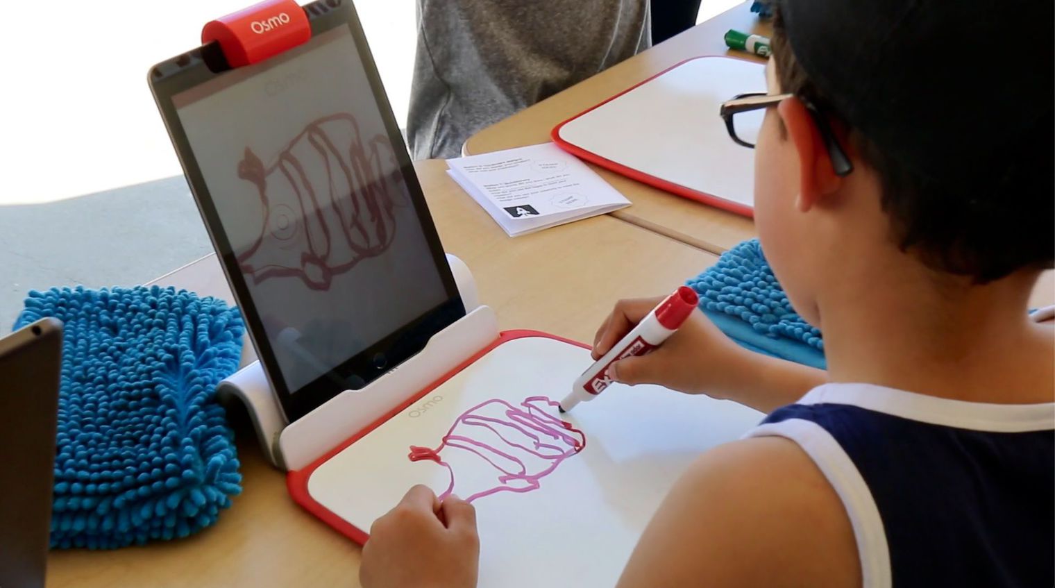 young boy drawing on paper as screen captures his art digitally