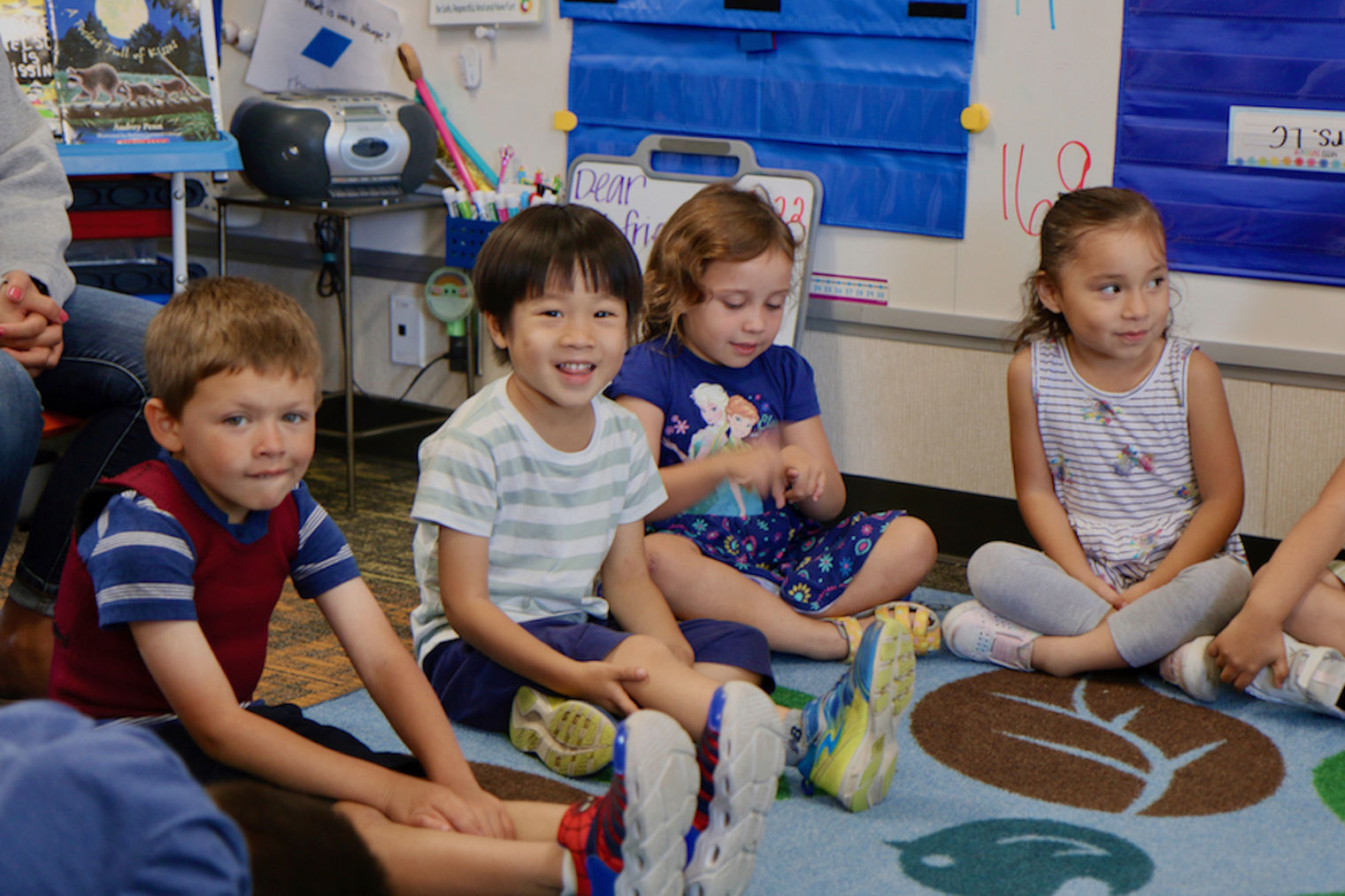 four kindergarten children sitting on the floor and smiling