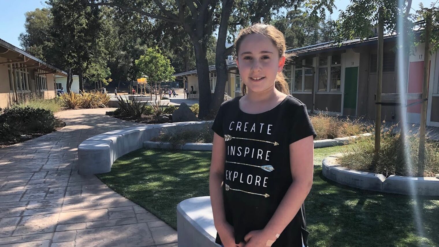 One girl standing, smiling at the camera and wearing a shirt that says Creating, Inspiring, Exploring.