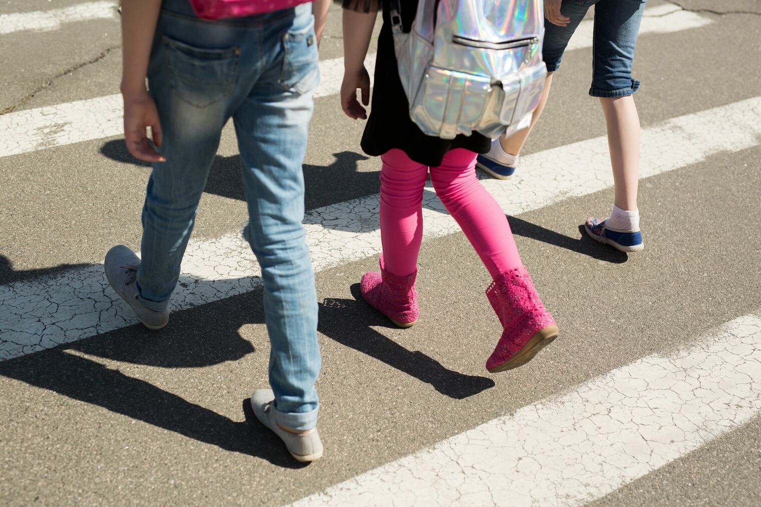 feet and legs of three children waking in the crosswalk of a street