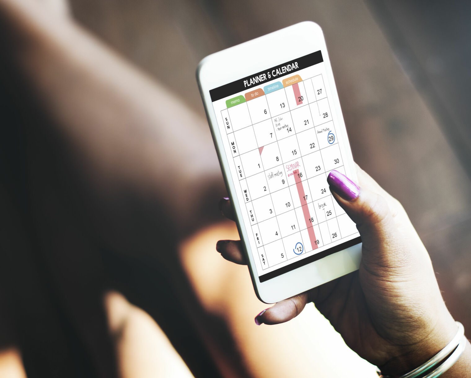 adult hand holding a mobile device showing a planner calendar